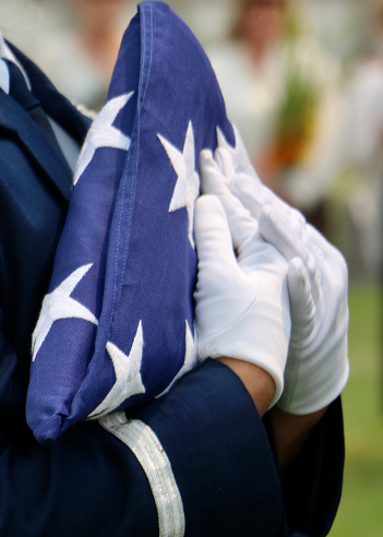 Closeup, male in blue dress uniform carrying tricorn folded American flag.