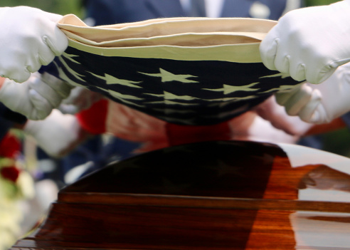 White gloved hands of US Military Honor Guardsmen folding American flag over casket