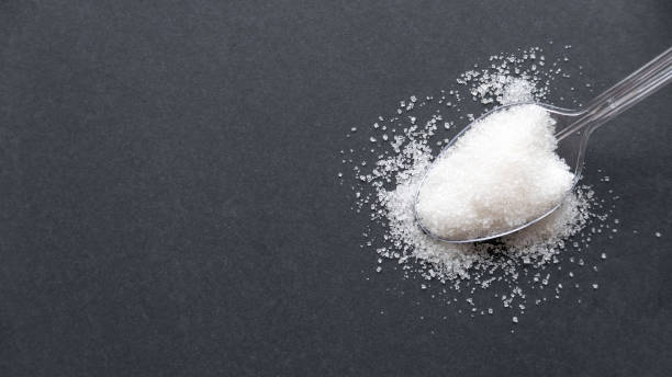 istock A white sugar in a transparent spoon on a black background with copy space. 1331975116