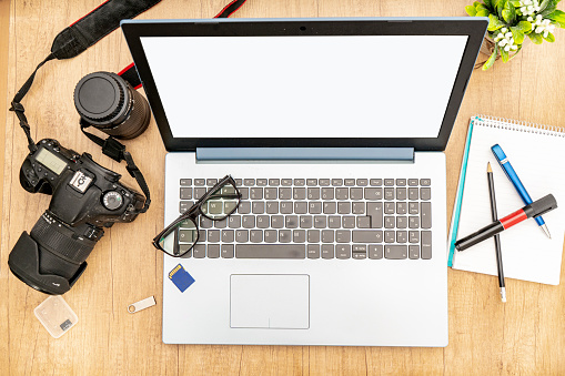 View of an open laptop with a reflex camera and a pair of glasses on the keyboard ready to work from home. Technology and communications concept.