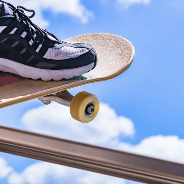 image from above of the feet of an African-American girl stepping on a skateboard with white sneakers with the shadow of a metal fence in the background