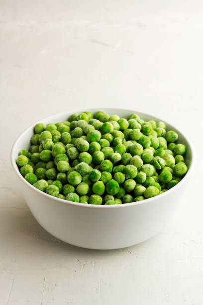 istock Frozen green peas in a white bowl on light background 1331979162