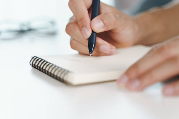 istock Close up of young man in casual cloth hands writing down on the notepad, notebook using ballpoint pen on the table. 1331979675