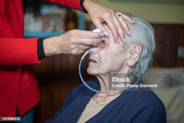 Family Caring For Family Daughter Putting Eye Drops In Elderly Moms Eyes With Ng Tube For Dysphagia Stock Photo - Download Image Now