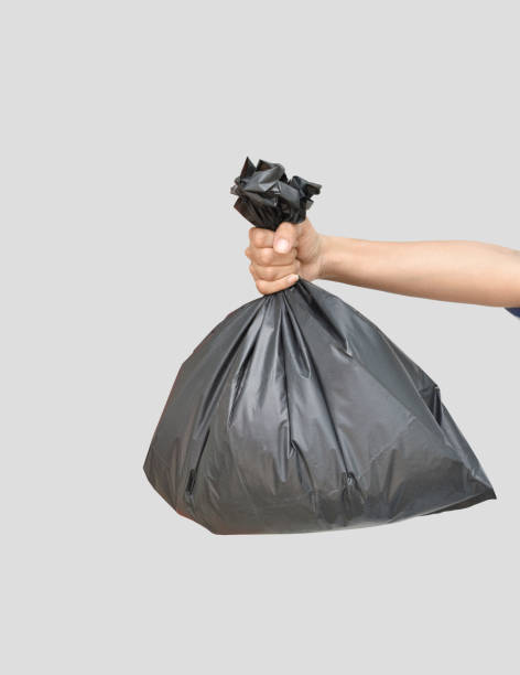 istock Hand holding a black garbage bag on grey background 1331980936
