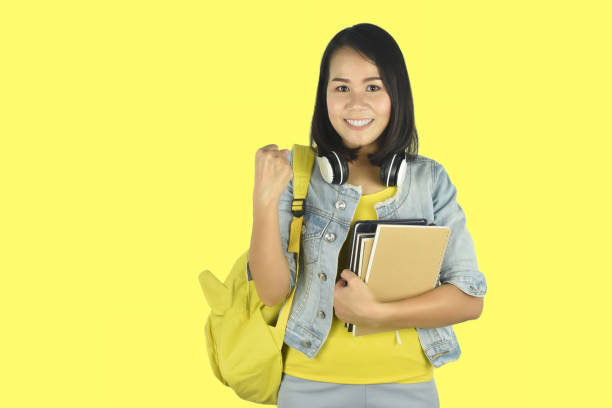 istock Woman student with backpack and hold notebooks showing yes gesture on yellow background studio portrait. 1331981079