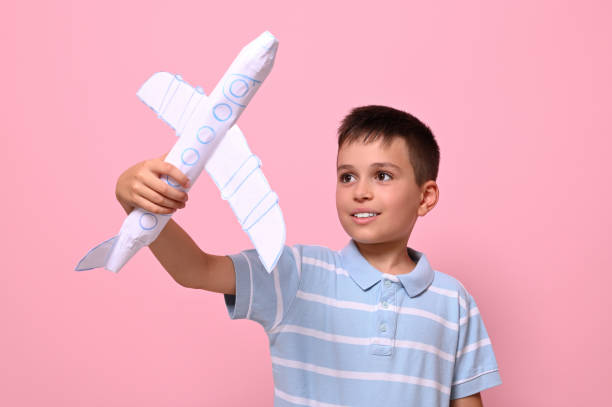 istock Handsome schoolboy playing with a paper airplane against pink background with copy space. Tourism, travel, geography knowledge concepts 1331981814