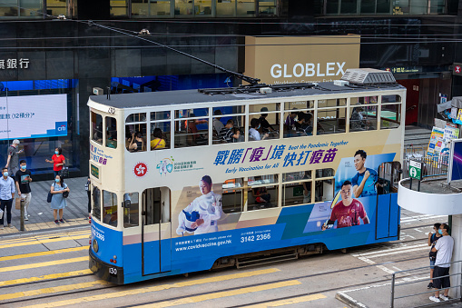 Hong Kong - August 2, 2021 : A tram featuring an advertisement for the COVID-19 Vaccination Programme travels along a road in Central, Hong Kong.