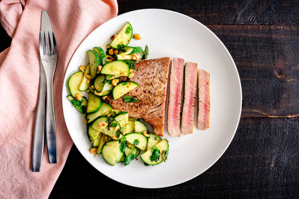 Tuna Steak with Cucumber-Peanut Salad Rare fish fillet served with cucumber and peanut salad as a side dish skipjack stock pictures, royalty-free photos & images