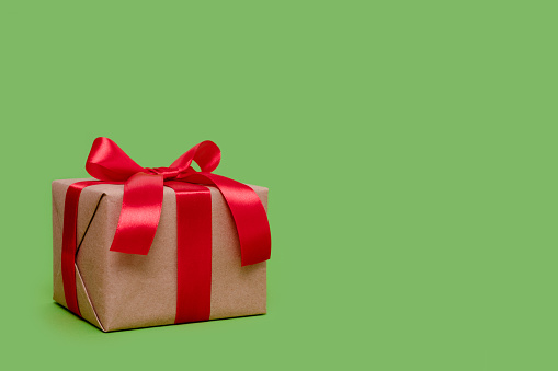 Gift box tied with red ribbon on a green background with copy space. Minimal composition.