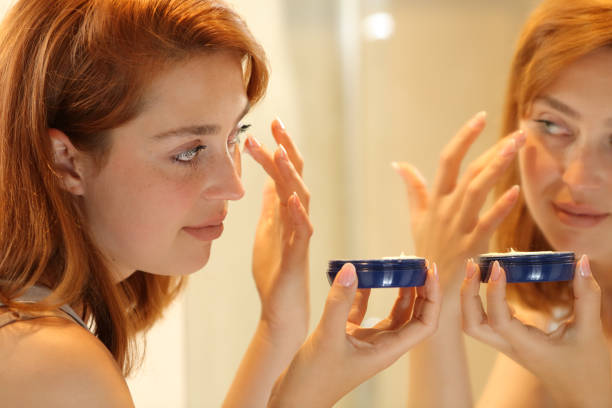 femme appliquant une crème hydratante dans des poches pour les yeux à la maison - human skin dry human face peeling photos et images de collection