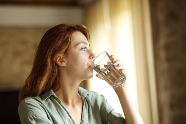Woman drinking water from glass at home stock photo