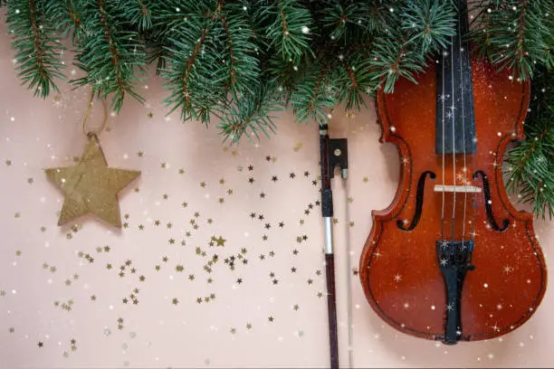 Old violin and fiddlestick, fir-tree branches with Christmas decor. Christmas, New Year's concept. Top view, close-up on pastel color background