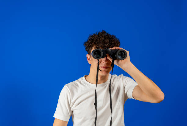 istock Young man over isolated blue background and looking in the distance with binoculars 1331991373