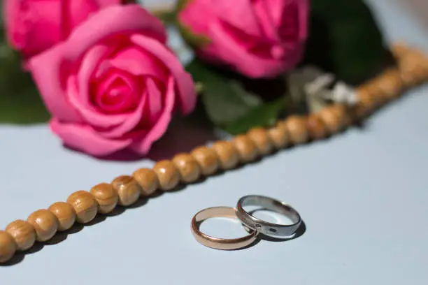 Gold and silver wedding ring, pink roses, tasbeeh rosary beads. Islamic wedding concept.