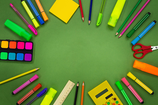Back to school. Stationery on green background. Markers, pencils, pens, scissors, calculator, ruler, paints, adhesive note. Places for text. Copy space
