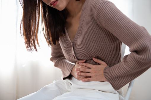 Concepto médico de la salud o de la vida diaria: El estómago cercano de la joven tiene un dolor de estómago o dolor de menstruación sentado en un sofá. photo