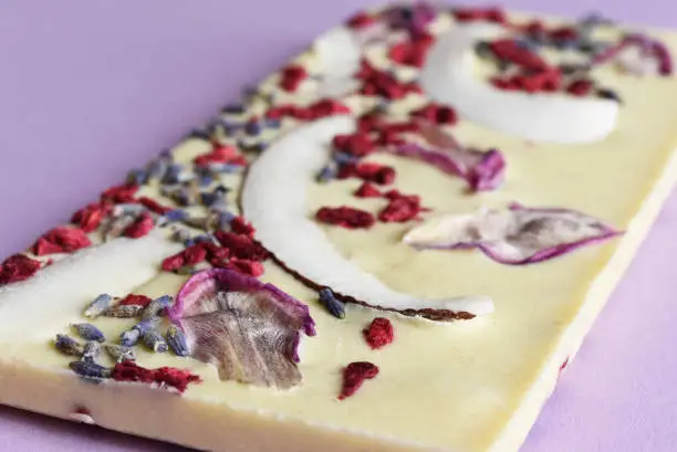 Photo of Handmade white chocolate with fillings: with nuts, rose petals, with coconut on a lilac background.