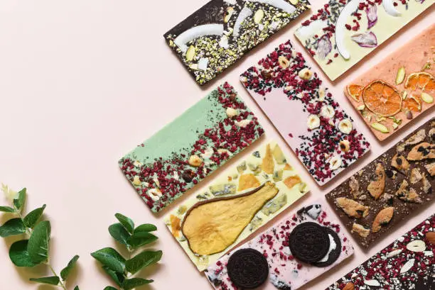 Photo of Handmade chocolate with different fillings: cookies, lavender, rose, orange, pear, coconut, walnut, candied fruit, cheese on a delicate beige background.