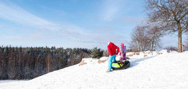 eine junge frau und ein 5-jähriges mädchen rutschen auf einem aufblasbaren kreis einen verschneiten berg hinunter. - child winter snow 4 5 years stock-fotos und bilder