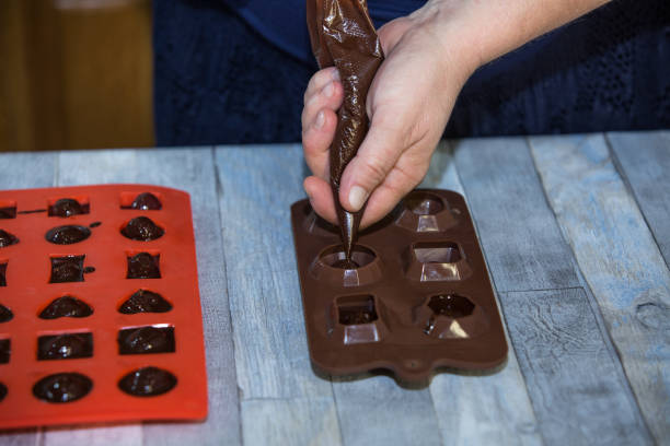 istock Step-by-step process of making chocolates from dark chocolate and cherries in cognac at home. A woman pours hot chocolate into candy molds with prepared cherries. Culinary blog concept. 1332002952