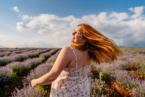 Young overweight smiling beautiful woman tousling hair in lavender field.