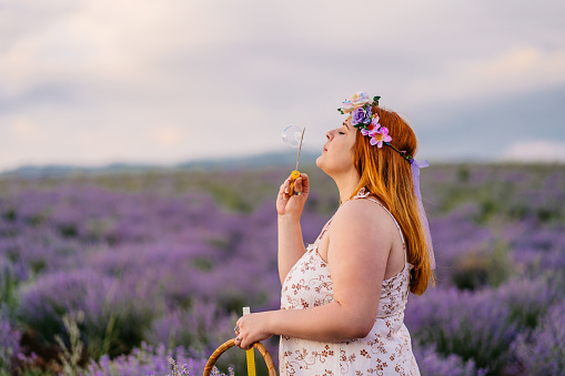 Overweight woman blowing soap bubbles in lavender field. Magnificent lavender field on the background. Magical sunset colors. Young woman having fun outdoor.