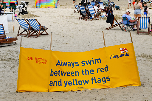 Weymouth, England - July 2021: RNLI sign advising visitors to swim between the red and yellow flags for safety reasons.