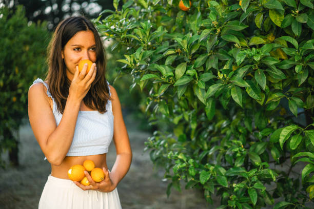 Young woman smells freshly picked oranges from tree