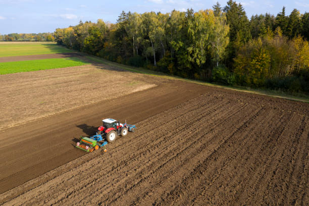 Tractor cultivating and sowing field A red, modern, agricultural tractor cultivating and sowing field in a beautiful, idyllic landscape, aerial view. overcasting stock pictures, royalty-free photos & images