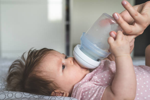 istock Side view on small caucasian baby four months old drinking milk formula while unknown woman mother is holding a bottle bottle 1332016722