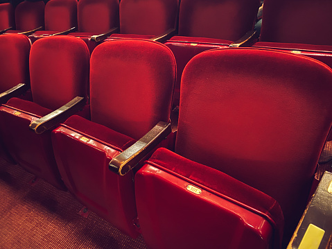 Empty cushioned red theater seats with gold numbers in movie theater cinema for viewing broadway show performances, movies and stage acting performances background