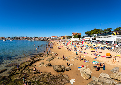View of the crowded pretty little beach named Praia da Duquesa along the beach promenade between the towns of Estoril and Cascais, nearby Lisbon, Portugal