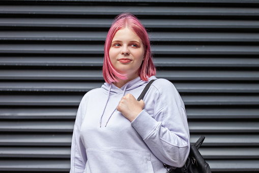 Outdoors portrait of a 20 year old woman in a purple hooded shirt with pink hair