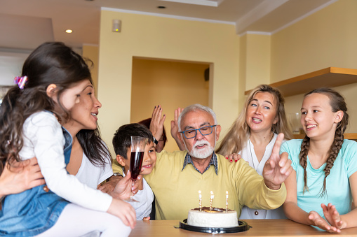 A Grandfather is Enjoying in Birthday Cake in Cheerful Atmosphere with Grandchildren and Other Family Members.