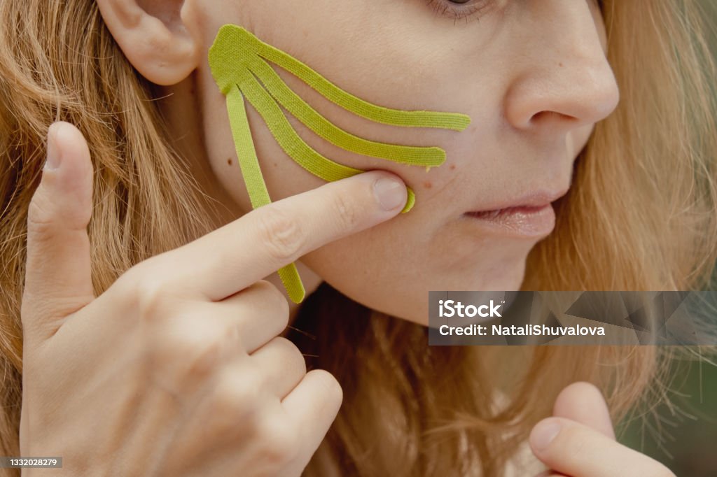 Young woman with green tapes on face. Face aesthetic taping. Attractive young woman with kinesiology tapes on forehead. Beautiful Woman With Kinesiology Facelift Tapes Filming Stock Photo