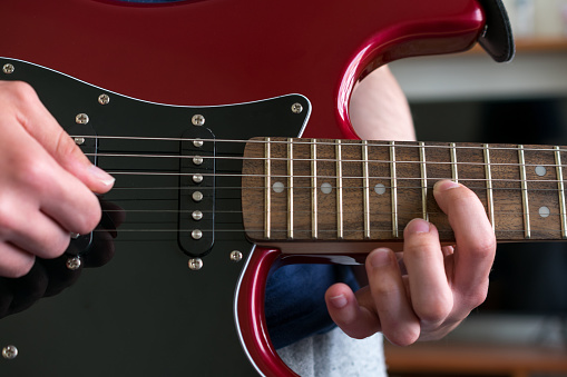 Close up view of a hand pressing the strings on an electric guitar, near the neck joint. Unrecognizable person playing the guitar, music concepts