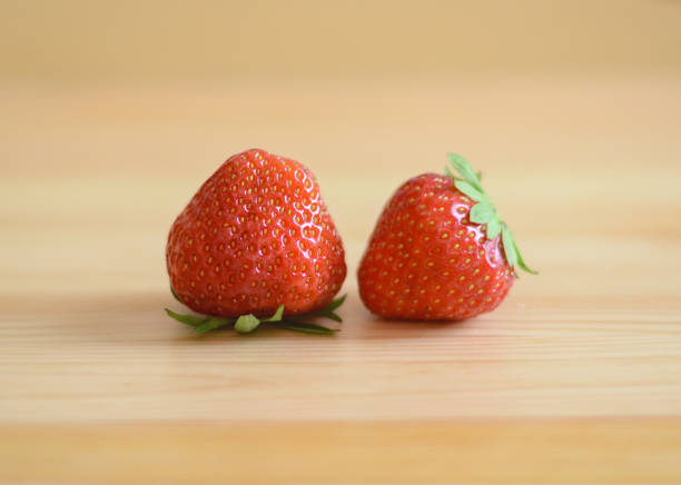 Two strawberries side by side with a wooden background stock photo