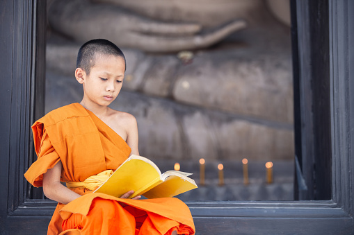 Young novice monk reading a book in Wat Phutthai Sawan Temple, Ayutthaya, Thailand