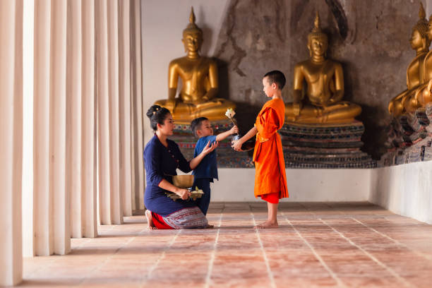 madre e figlio famiglia buddisti thailandesi stanno dando elemosina ai novizi che fanno merito con monaco nel tempio wat phutthai sawan, ayutthaya - wat pho foto e immagini stock