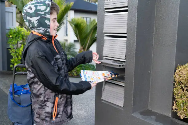 Auckland - New Zealand -  19  July 2021; Young boy earning a small income by delivering advertising brochures to private letterboxes in residential suburb