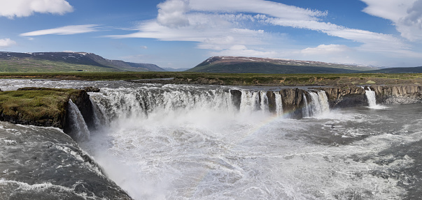 Goðafoss Waterfall Summer Panorama. View over the famous Godafoss Falls -  icelandic “Waterfall of the Gods” in summer under sunny blue skyscape. The water of the river Skjálfandafljót falls from a height of 12m over a width of 30m. Akureyri, Fossholl, Northern Icelandic Highlands, Iceland, Nordic Countries, Europe.