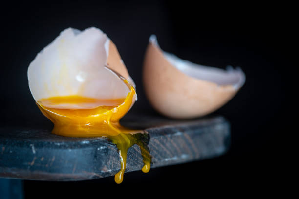 istock Broken egg shell with dripping yolk on wooden cutting board on black background, close up 1332067580