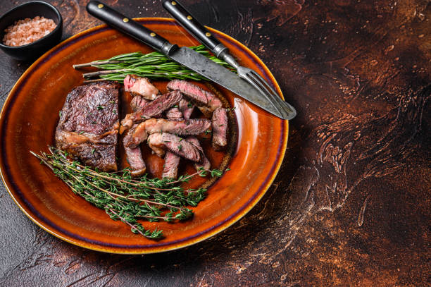 istock Grilled sliced rib eye or ribeye beef meat steak on a rustic plate. Dark background. Top view. Copy space 1332069948