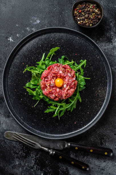 istock Beef tartar with a quail egg served on a black stone plate.. Black background. Top view 1332070881