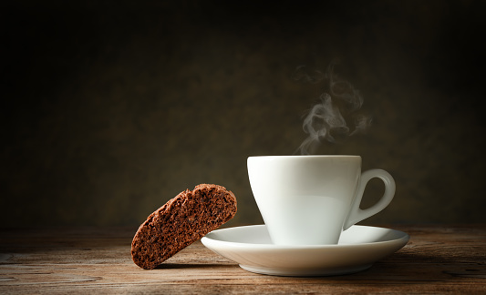 Cup of coffee and a biscuit on wooden table with dark background, copy space.