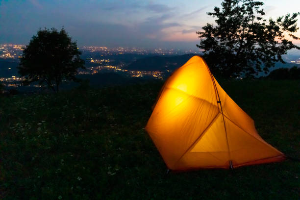 istock Illuminated camping tent on hill top, night view of city below 1332071926