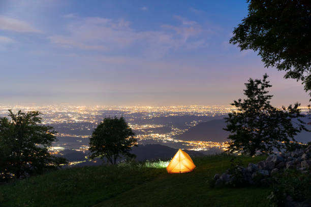 istock Illuminated camping tent on hill top, night view of city below 1332071955