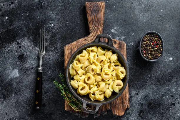 Italian tortellini pasta with cheese sauce in a pan. Black background. Top view.
