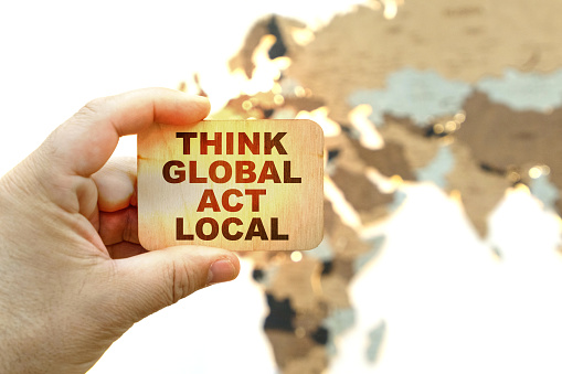 Business concept. Against the background of the world map, a man holds a sign with the inscription - Think global act local